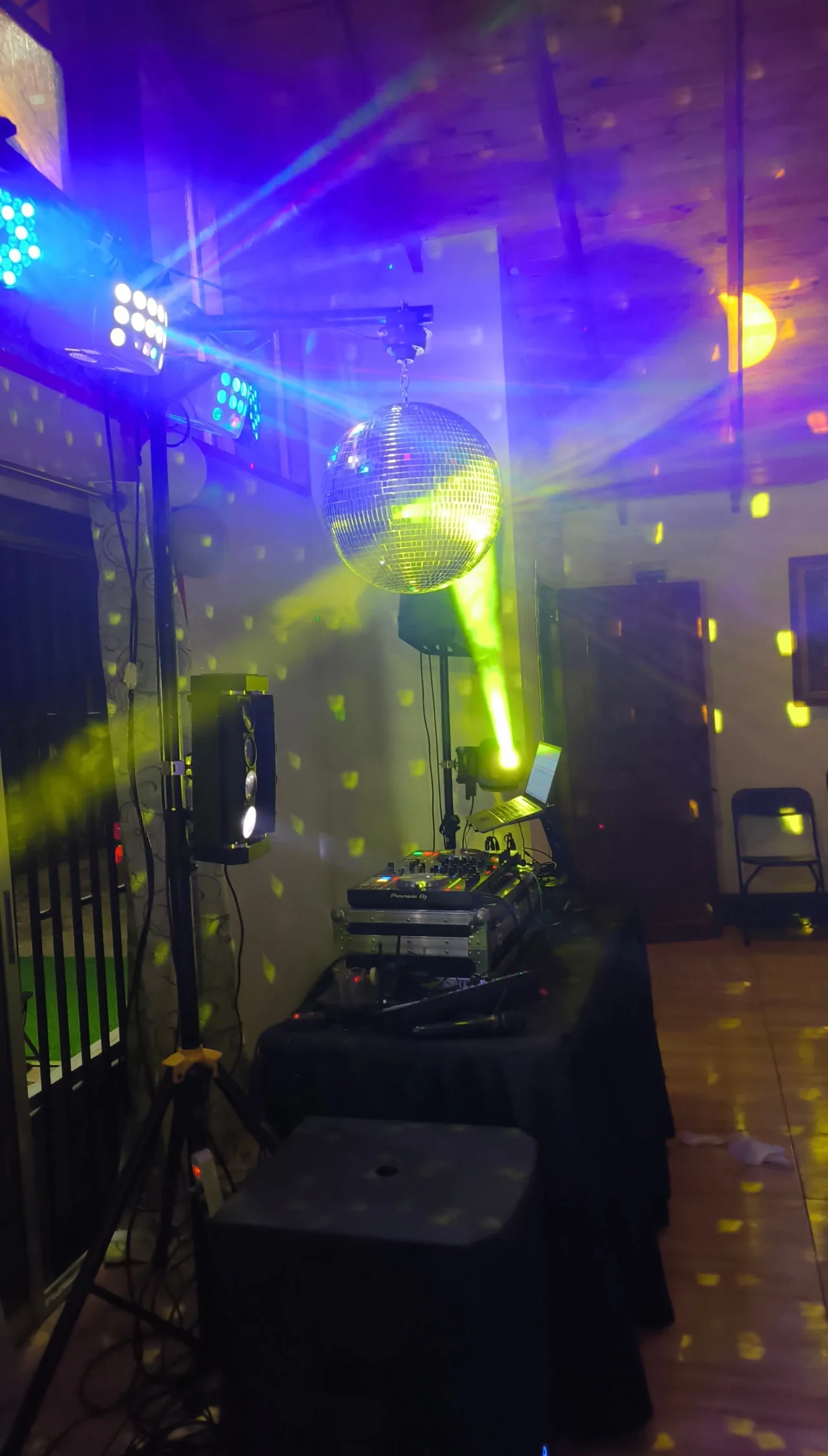 Montaje de DJ con consola, parlantes, bola de espejos y luces verdes y violetas en un salón