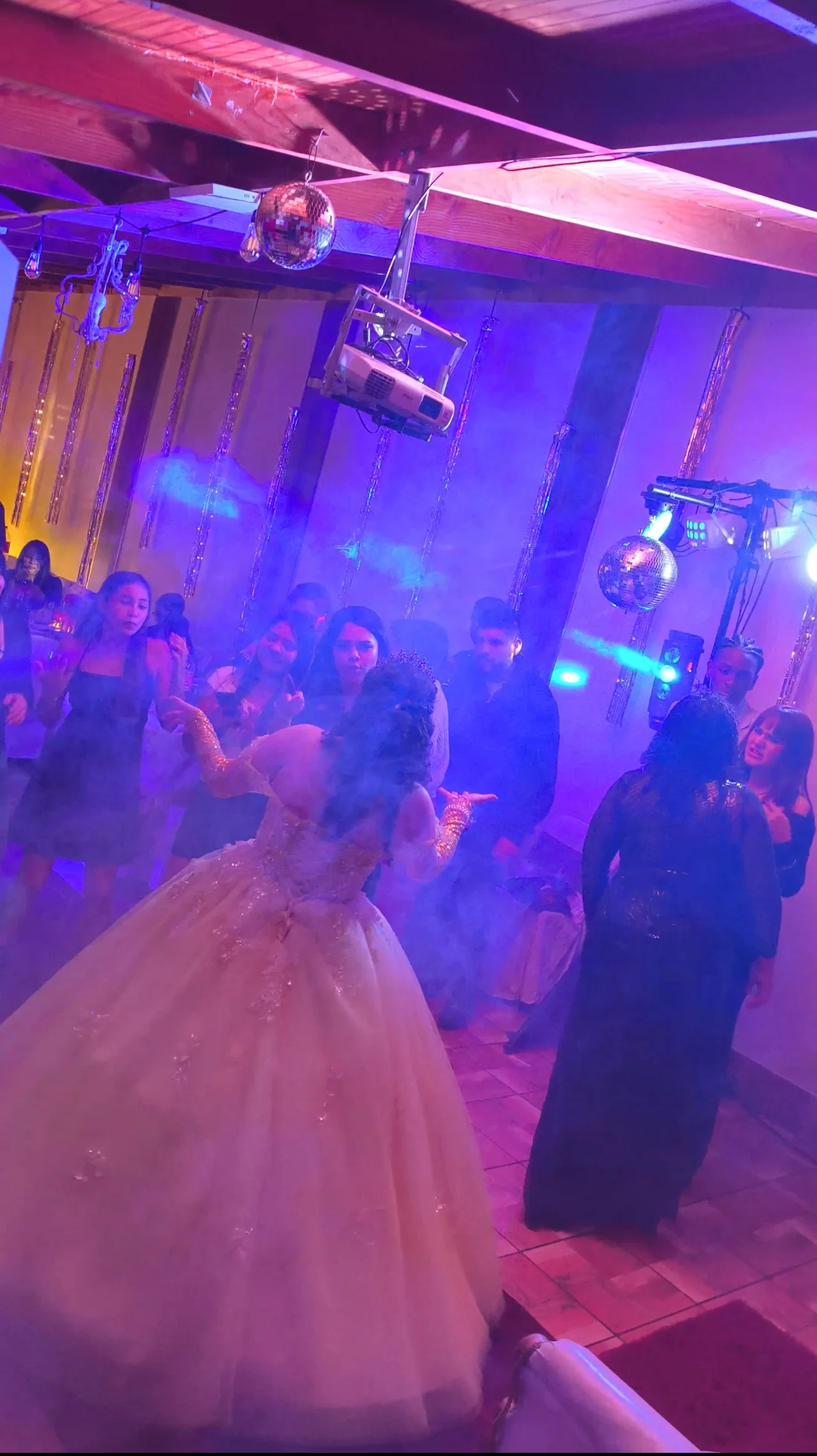 Quinceañera e invitados en la pista de baile con humo e iluminación violeta y azul