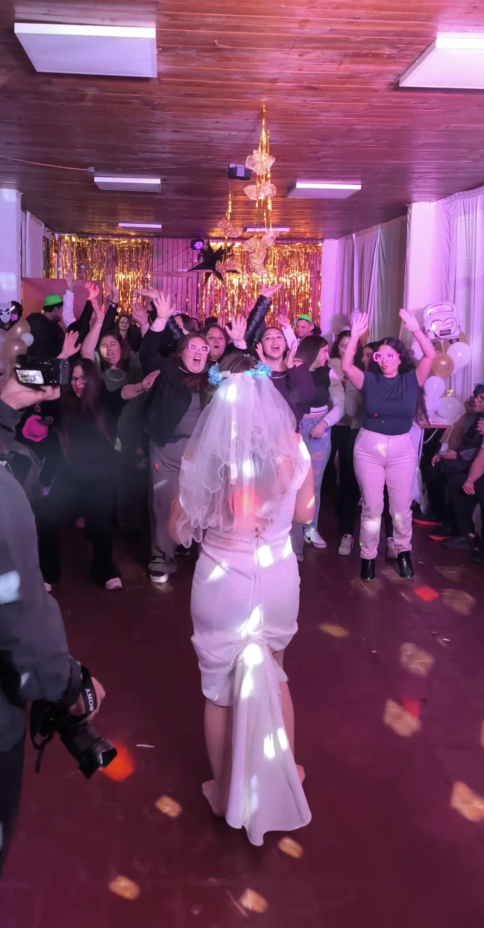 Novia e invitados celebrando en la pista de baile de un salón iluminado en tonos magenta