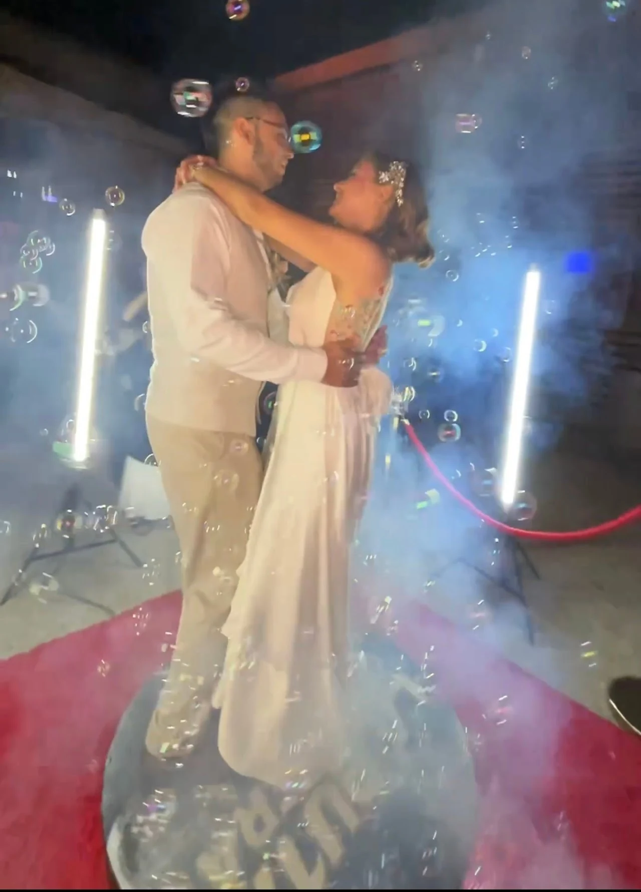 Novios bailando sobre una plataforma rodeados de humo, luces y burbujas