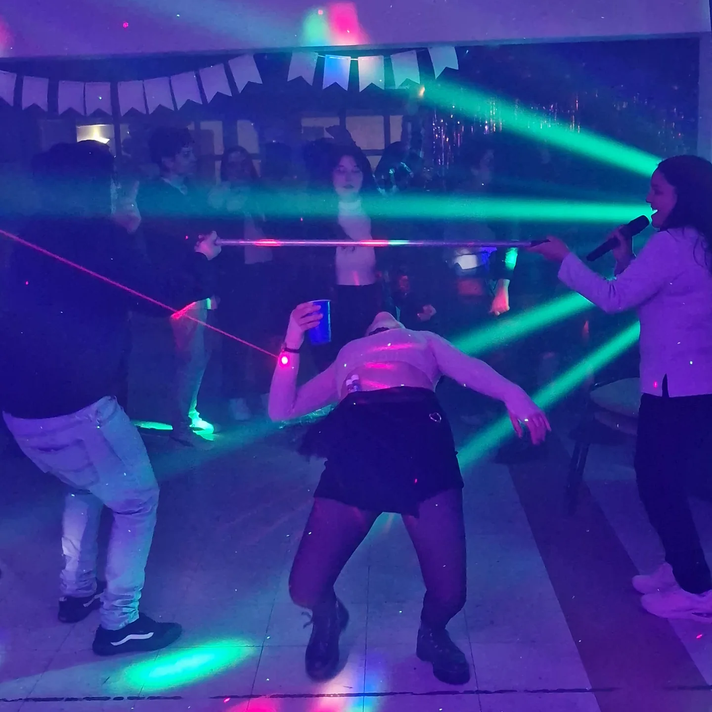 Animadora con micrófono e invitados participando en un juego de limbo con luces de fiesta