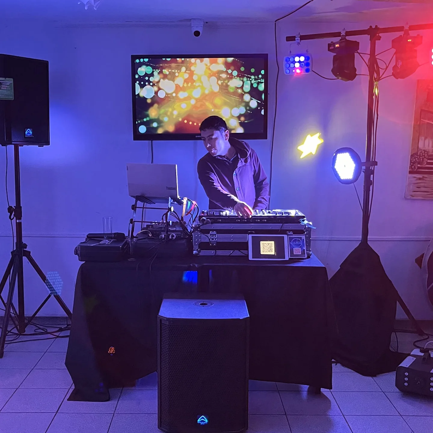 DJ trabajando en su consola con parlantes, pantalla y luces instaladas en el salón